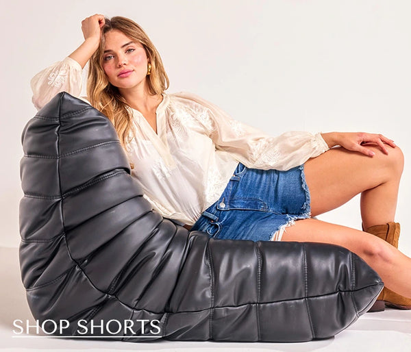 Woman sitting on a large black cushion with 'Shop Shorts' text overlay